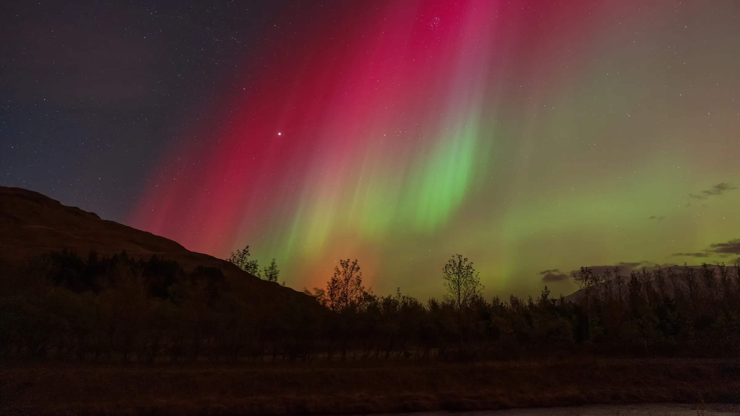Aurora boreal roja y verde sobre montañas y bosque en Islandia